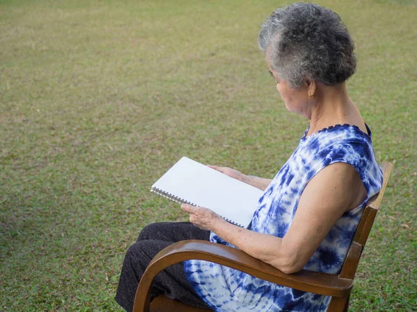 Mulher Sênior Sentada Lendo Livro Cadeira Jardim Espaço Para Sms — Fotografia de Stock