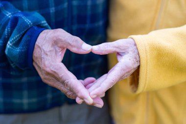 Yaşlı çiftin parmaklarıyla kalp yaparken çekilmiş yakın çekimi. Yaşlılar ve aşk kavramı.