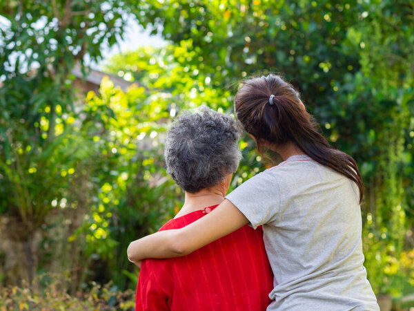 Back view of a young woman hugging her grandmother in the garden. Concept of aged people and healthcare.