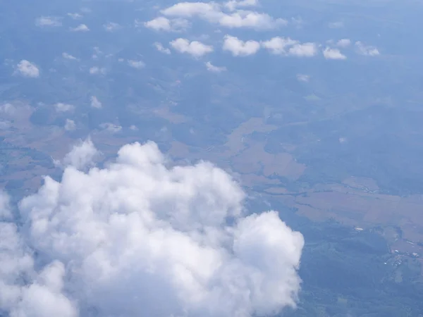 Aerial view of lands and clouds seen through airplane window.