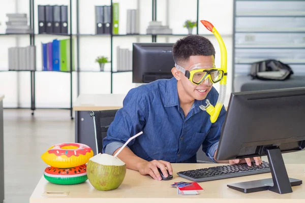 Young man wearing a diving mask yellow while sitting working in the office. He is dream of the sea because the holiday coming soon. Concept of people and holiday.