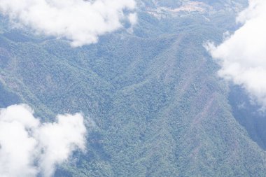 Uçak penceresinden görünen dağların, gökyüzünün ve bulutların havadan görünüşü.