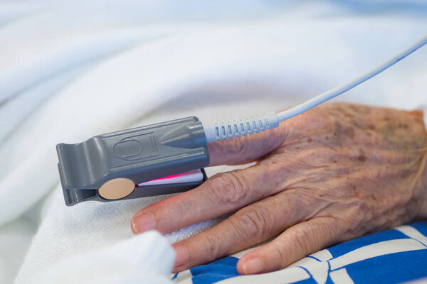 Крупный план оксиметра крови и пульса от пальца пожилого пациента в палате больницы. Концепция пожилых людей и здравоохранения.