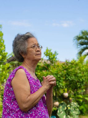 Yaşlı bir Asyalı kadın bahçede dururken dua ediyor. Mesaj için yer var. Yaşlılar ve sağlık hizmetleri kavramı.