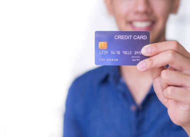 Mavi gömlekli genç adam gülümsüyor ve online alışverişe hazırlanmak için mavi bir kredi kartı gösteriyor. Mesaj için yer var. Finans ve e-ticaret kavramı.