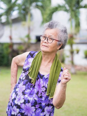 Yaşlı bir Asyalı kadın, kısa gri saçlı, günlük giysiler giyen, gülümseyen ve bahçede dikilen bir kadın. Mesaj için yer var. Yaşlılar ve sağlık hizmetleri kavramı.