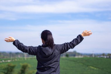 Back view of a woman hands up while standing looking at the tea plantation. Space for text. Relaxation concept.