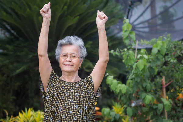 Portrait of an elderly woman exercise while standing in a garden. A beautiful senior woman short with gray hair is happy and healthy. Concept of aged people and healthcare.