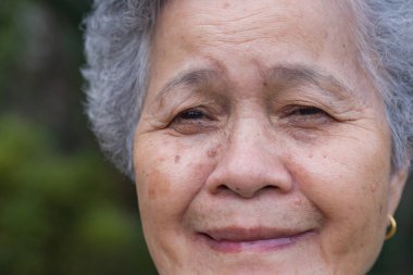 Altın bir küpe takan, gülümseyen ve kameraya bakan yaşlı bir kadının yan görüntüsü. Yaşlılar ve sağlık hizmetleri kavramı.