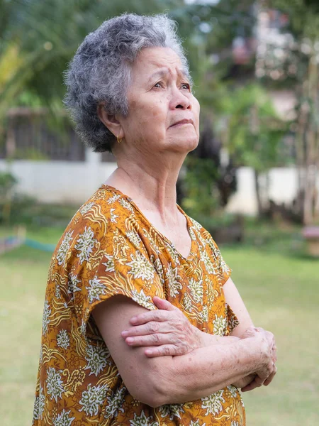 Portrait of a senior woman with arms raised and looking up while standing in a garden. Concept of aged people and healthcare.