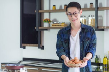 Genç adam mutfakta pişirmek için organik yumurta dolu bir sepet gösteriyor. Yumurtalar vücuda yararlıdır. Protein vücudun sağlıklı olmasına yardımcı olur. Mesaj için yer var. Sağlıklı yiyecekler konsepti.