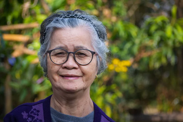 Portrait of a senior woman with short gray hair wearing glasses, smiling, and looking at the camera while standing outdoors. Space for text. Concept of aged people and healthcare.