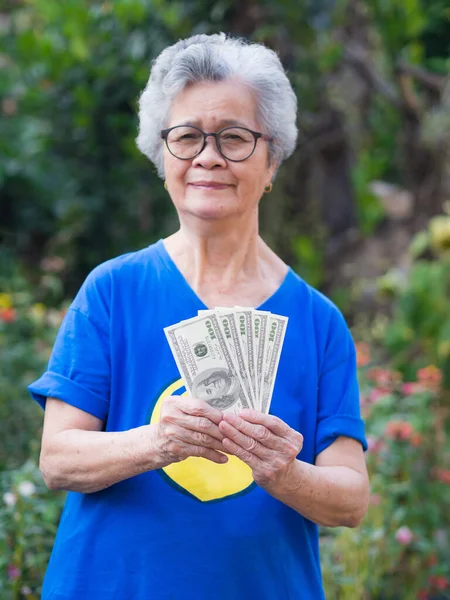 A portrait of an elderly woman short white hair wearing glasses smiling with arms crossed and looking at camera while standing in a garden. Slective focus. Concept of old people and healthcare