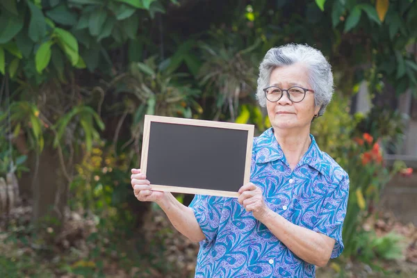 A portrait of an elderly woman holding a blackboard while standing in a garden.Concept of old people and health care
