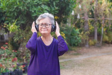 Kablosuz kulaklık takan yaşlı bir kadın favori bir şarkıyı dinliyor ve bahçede mutlu bir şekilde gülümsüyor. Asyalı son sınıf öğrencisi, kısa beyaz saçlı, müzikten hoşlanıyor. Akıl sağlığı konsepti