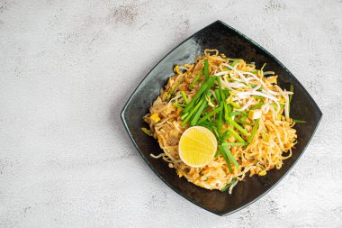 Pad Thai, sebze ve limon dilimleri ile servis edilir. Siyah tabakta gri çimento arka planda. Tayland yemekleri meşhurdur. Kopyalama alanı olan üst görünüm. Geleneksel Tayland yemekleri kavramı