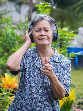 Kulaklık takan yaşlı bir kadının portresi. Bahçede dikilirken parmaklarını gösteriyor. Asyalı son sınıf öğrencisi, kısa beyaz saçlı, müzikten hoşlanıyor. Yaşlılar ve akıl sağlığı kavramı
