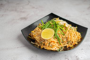 Pad Thai, sebze ve limon dilimleri ile servis edilir. Siyah tabakta gri çimento arka planda. Tayland yemekleri meşhurdur. Kopyalama alanı olan üst görünüm. Geleneksel Tayland yemekleri kavramı