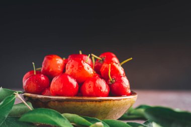 Siyah duvarda güneş ışığı olan bir seramik kasede olgun kırmızı kirazlar. Mesaj için yer var. Tatlı organik meyveler. Sağlıklı meyve kavramı