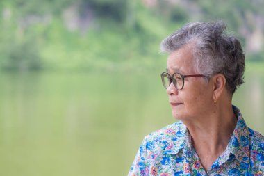 Yaşlı bir Asyalı kadının parkta dikilirken gülümseyip bakışlarını kaçırması. Yaşlılar ve sağlık hizmetleri kavramı