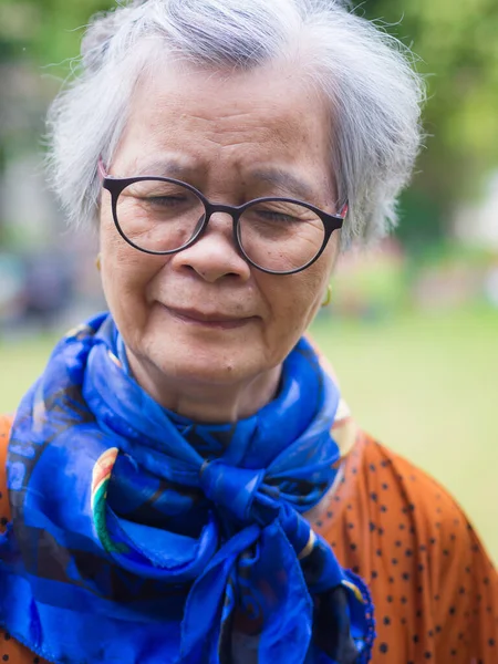 Portrait of a senior Asian woman wearing eyeglasses and looking down while standing in a garden while standing in a garden. Concept of old people and healthcare