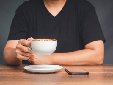 Genç bir adam masada otururken bir fincan kahve tutuyor. Yakın plan fotoğraf. İçecek ve rahatlama kavramı