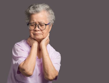 Boyun ağrısı çeken yaşlı bir kadın gri bir arka planda duruyor. Mesaj için yer var. Yaşlılar ve sağlık konsepti