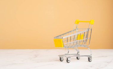 İş ve e-ticaret kavramı. Mermer bir masada turuncu arka planı olan boş bir alışveriş arabası. Metin için boşluk