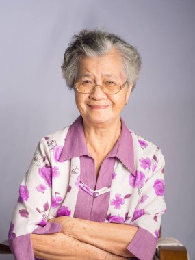 Kısa beyaz saçlı, yaşlı, güzel bir Asyalı kadın stüdyoda gri bir arka planda dururken kameraya gülümsüyor. Mesaj için yer var. Yaşlılar ve rahatlama konsepti