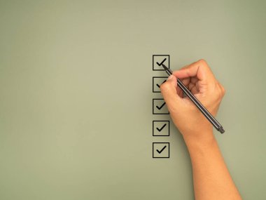 Kontrol listesi konsepti. Yeşil arkaplandaki kontrol listesi kutusundaki renkli siyah işaretler. Yakın plan, elinde kalem ve kontrol listesi var. Mesaj için yer var. Üst görünüm