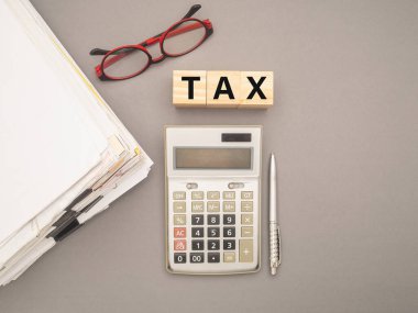 Klipsli, gözlüklü, hesap makineli ve gri arkaplanlı vergisiz tahta küplü dokümanlar. Mesaj için yer var. Üst Manzara. Vergi formları ve hesaplamalarında yardım