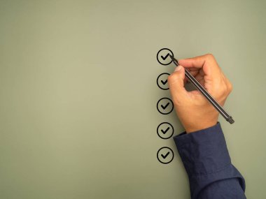 Kontrol listesi konsepti. Yeşil arkaplandaki kontrol listesi kutusundaki renkli siyah işaretler. Yakın plan, elinde kalem ve kontrol listesi var. Mesaj için yer var. Üst görünüm