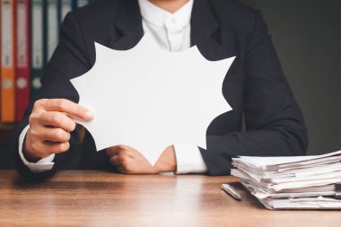 Konuşma balonu konsepti. Ofisteki masada otururken elinde boş beyaz bir konuşma balonu tutan takım elbiseli bir iş adamının yakın çekimi. Metin için boşluk