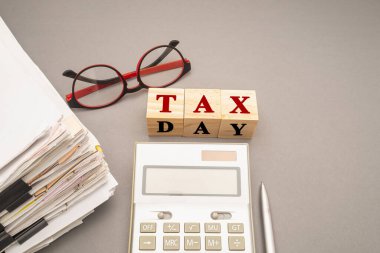 Klipsli, gözlüklü, hesap makineli ve gri arkaplanlı vergisiz tahta küplü dokümanlar. Mesaj için yer var. Üst Manzara. Vergi formları ve hesaplamalarında yardım