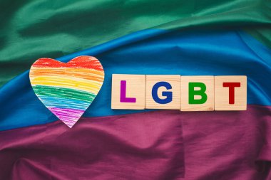 Gökkuşağı bayrağı ya da LGBT bayrağı üzerinde LGBT harfleri olan kağıt ve ahşap küplerden yapılmış bir gökkuşağı kalp sembolü. Gurur ayı. LGBTQ+. Cinsiyet çeşitliliği kavramı