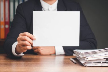 Ofisteki masada otururken elinde boş bir beyaz kağıt tutan takım elbiseli bir iş adamının yakın çekimi. Metin için boşluk
