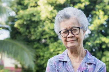 Kısa gri saçlı, güzel, yaşlı Asyalı kadın bahçede dururken kameraya gülümseyerek bakıyor. Mesaj için yer var. Yaşlılar ve rahatlama konsepti