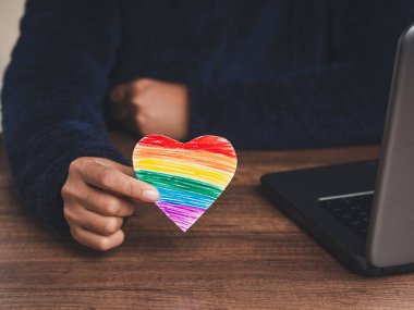 Yakın plan, kağıttan yapılmış gökkuşağı kalbini tutuyor. Cinsiyet çeşitliliği kavramı