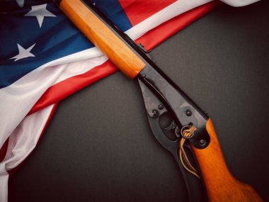 Siyah arka planda Amerikan bayrağı üzerinde bir av tüfeğinin üst görüntüsü. Mesaj için yer var. Yakın plan fotoğraf.