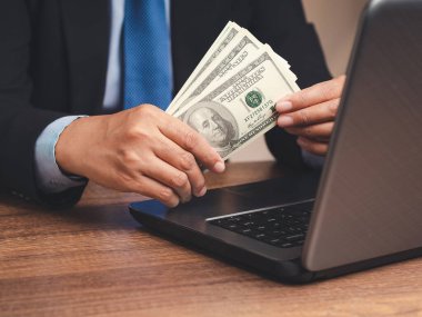 Kişisel kredi konsepti. Ofis fotoğrafında otururken takım elbiseli bir işadamı elinde Amerikan doları banknotları tutuyor. Para ve finans