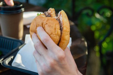 Elin ısırılmış bir hamburgeri tutuyor.