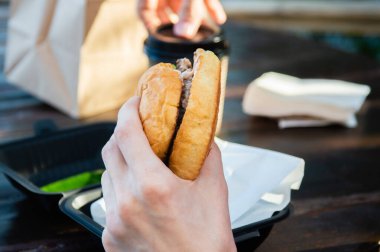 Elin ısırılmış bir hamburgeri tutuyor.