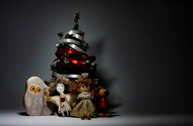 Beyaz ve kırmızı çizgilerle süslenmiş farklı dört oyuncağın yatay kavramsal stüdyo fotoğrafı gri arka planda küçük bir Noel ağacı.