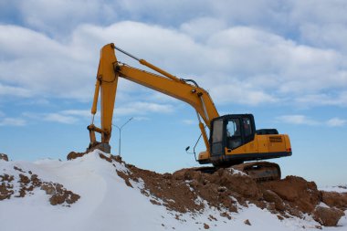 Dalgalanma sırasında çekilmiş yatay fotoğraf sarı kepçe kazıcı, kumlu tepenin üzerinde duruyor kışın beyaz bulutlarla birlikte