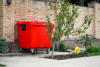 Parlak kırmızı çöp tenekesi güzel bir tuğla çitin yanında.