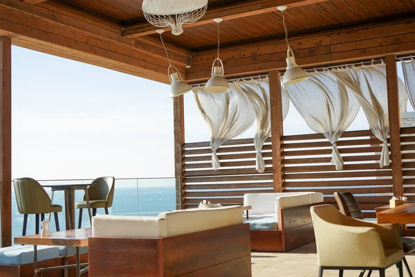 Kafenin yaz terasında güçlü sıcak bir rüzgar perdeleri uçuruyor.