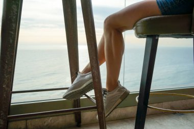 Bir kadın yüksek bar taburesinde bir masada oturuyor.