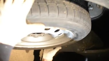 Dikey video tamircisi bijon somunlarını pnömatik bir anahtar ile söküyor. Uzmanlar bir aracın bileşenini tamir etmek için tekerleği çıkarırlar. Sezonluk lastik değişimi.