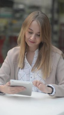 Dikey video bir kafede çalışan bir kız sitesi uzmanı sosyal ağlara, postalara, mektuplara ve tabletlere bakar. Gülümseyen pozitifler modern teknolojileri kapalı mekanda kullanıyor.