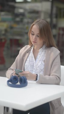 Dikey video kulaklı ve akıllı telefonlu güzel kız müzik dinliyor ya da şehir merkezindeki kafe alışveriş merkezinde film izliyor.